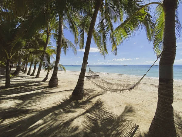 Relaxing hammock in a palm forest. Beautiful landscape on a white sandy beach. Boats on the background of the turquoise sea and the blue sky. The concept of travel and leisure.