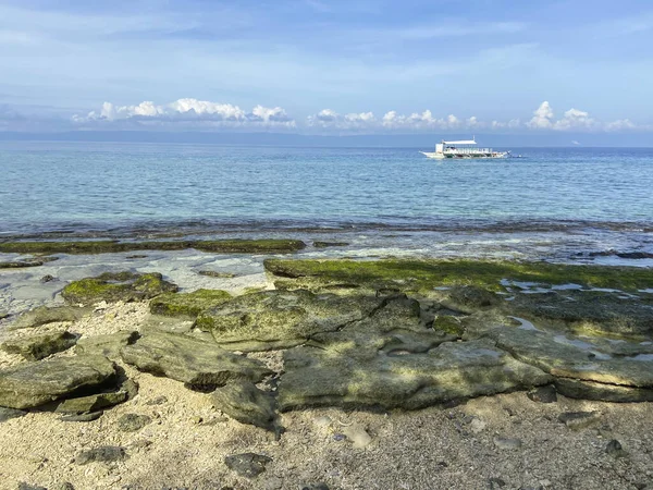 Taş tabaklar, kum ve mavi denizle güzel bir sahil manzarası. Arka planda seyreden bir gemi gökyüzü ve beyaz bulutlar. Seyahat ve macera.