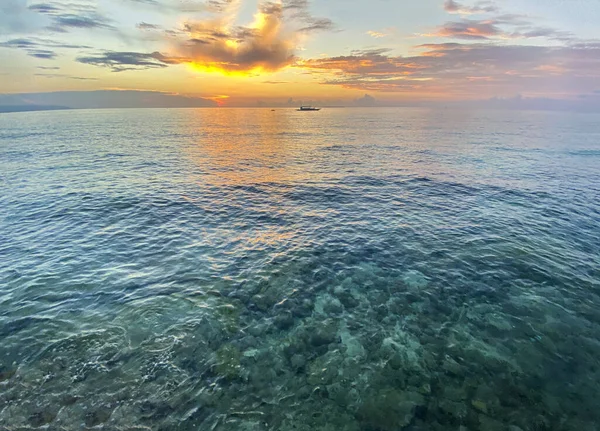 İnanılmaz güzel bir gün batımı, şafak. Deniz kenarında şeffaf turkuaz sularda büyük taşlar. Ufuktaki tekneler.