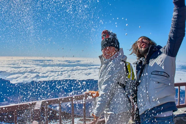 Chica y chico divirtiéndose con nieve en invierno en la cima de la montaña con un fondo azul — Foto de Stock