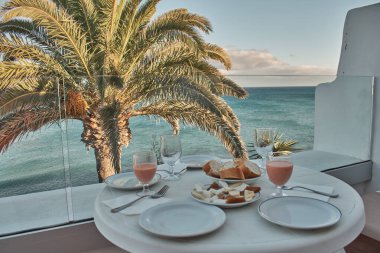 Palmiye ağaçları ve deniz manzaralı bir terasta yemek hazırlığı.
