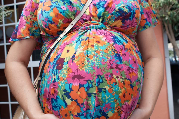 Ön planda çiçekli elbisesi olan hamile bir kızın midesi.