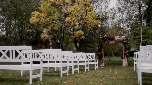 秋の森には花の装飾が施されたアーチが登録されており 隣には白いヴィンテージのベンチがあります — ストック動画