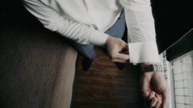 Adam beyaz bir gömlek giyip pencerede kelepçeleri düzeltiyor.