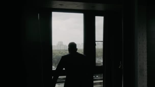 バックライトの男はカメラに背を向けて窓にジャケットを置きます — ストック動画
