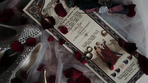 Bruiloft Uitnodiging Ligt Een Tafel Bezaaid Met Rozenblaadjes Waarop Ringen — Stockvideo