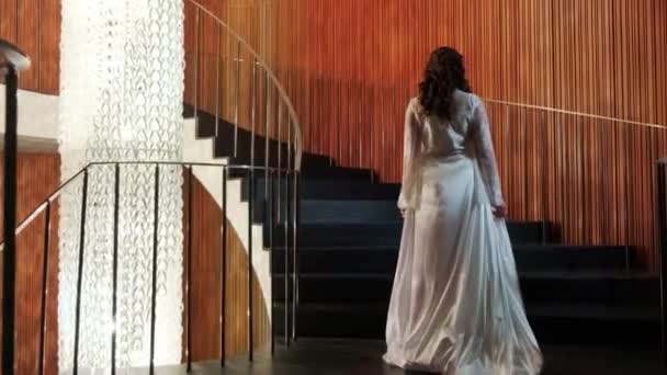 長い白いバスローブを着た若い女性が上の階に階段を登る — ストック動画