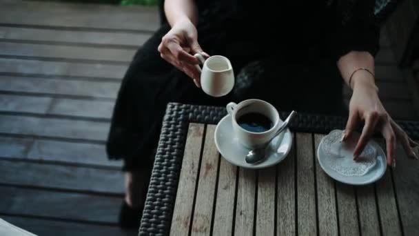 Önts Tejszínt Kávéba Egy Fekete Fürdőköpenyes Lány Aki Egy Asztalnál — Stock videók