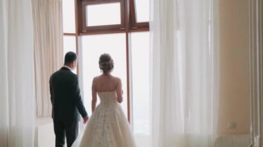 Gelin ve damat pencereden dışarı bakar sırtlarını döner ve birbirlerinin ellerini tutarlar.