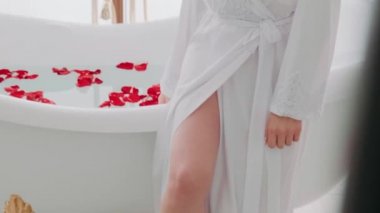 Küvette oturmuş su test eden çekici genç bir kadın. Suda Sevgililer Günü 'nde kırmızı gül yaprakları. Bir kadın için aşk.