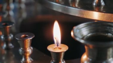 Small burning candle in a large candle holder stands in an Orthodox Church, people walk in background, they are christen and perform Orthodox sacred