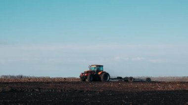  Baharda bir tarladaki traktör açık mavi gökyüzüne kara toprağı sürükler. Tarımsal makineler üzerinde çalışıyorum. Tarlayı ekme hazırlığı.
