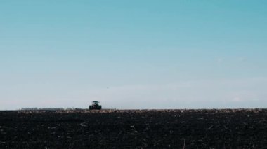  Baharda bir tarladaki traktör açık mavi gökyüzüne kara toprağı sürükler. Tarımsal makineler üzerinde çalışıyorum. Tarlayı ekme hazırlığı.