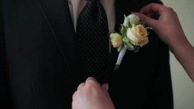 Ceketli bir adam beyaz düğmeli bir gül asıyor.