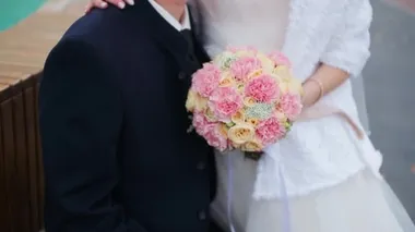 Düğünde takım elbiseli bir damat pembe buketli ve beyaz elbiseli hamile bir geline sarılıyor. Bir adam hamile karnını okşar.