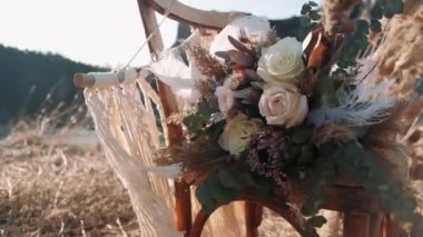 Boho düğün buketi. Rüzgarda sallanan büyük beyaz bir tüy. Boho düğün buketi doğada bir sandalyede yatıyor.
