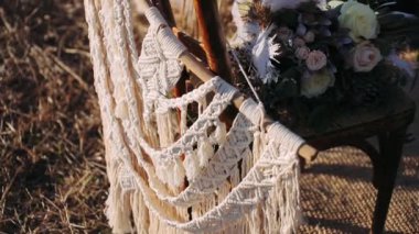 Boho düğün buketi. Rüzgarda sallanan büyük beyaz bir tüy. Boho düğün buketi doğada bir sandalyede yatıyor.