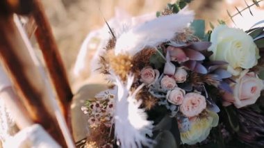 Boho düğün buketi. Rüzgarda sallanan büyük beyaz bir tüy. Boho düğün buketi doğada bir sandalyede yatıyor.