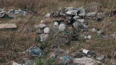 Yerdeki plastik çöpler. İnsanların neden olduğu çevreye zarar veriyorlar. Yerde çöp var. Genç yeşil çimenlerin yanında..