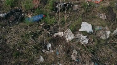 Yerdeki plastik çöpler. İnsanların neden olduğu çevreye zarar veriyorlar. Yerde çöp var. Genç yeşil çimenlerin yanında..