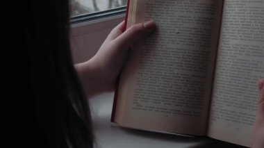 Kendi kendini eğitme. Evde ders çalışıyorum. Bir kız yeşil baharda pencerenin yanında bir kitap okuyor..