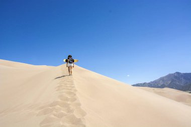 Kum tepeciğinde yürüyen kumlu bir kadın.