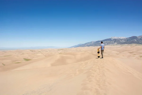 young man with sand board on sand dune in great sand dunes national park colorado