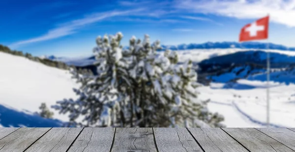 Dřevěná police stůl zimní hora panorama švýcarské vlajky sníh pokryté hory s borovicemi — Stock fotografie
