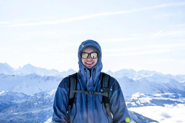 Montanhista mochileiro sorrindo no cume contra azul nevado camadas de montanha no inverno. sol, céu azul — Fotografia de Stock
