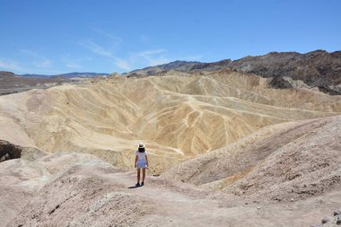 Güneşli bir günde, yazın ölüm vadisi çölünde duran şapkalı bir kadın turist.