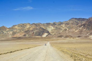 Badwater Havzası 'ndaki Ölüm Vadisi Ulusal Parkı' nda sarı çakıl yolu. Arka planda dağ sırası var. güneşli, mavi gökyüzü, yaz