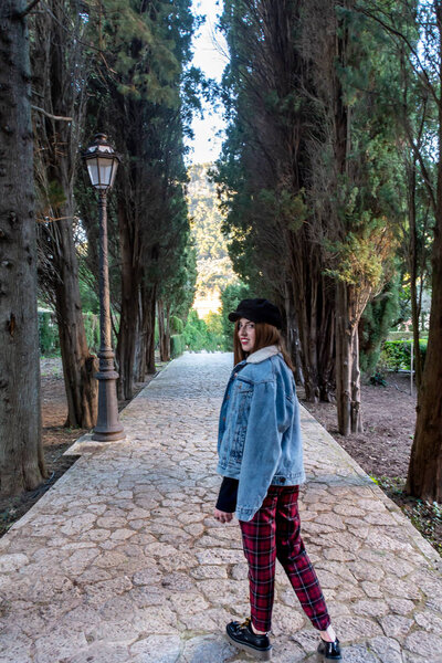Милая молодая девушка в джинсовой куртке и красных клетчатых брюках, на открытом воздухе Ла-Картуха в Вальдемосса, Мальорка глядя в сторону
