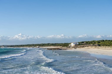 Gözetleme, Campos. Mayorka 'da Akdeniz plajı, rüzgarlı bir günde, birkaç dalgalı deniz ve kumda yürüyen iki kişi..