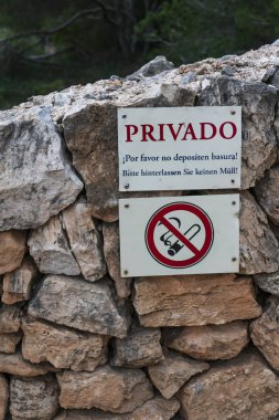 Çevre uyarı levhası taştan bir duvarda, Almanca ve İspanyolca dillerinde: 