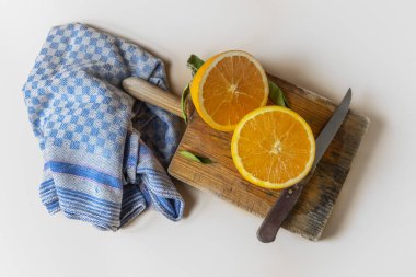 Orange cut in half, on a cutting board, next to a blue dishcloth, on a white background clipart