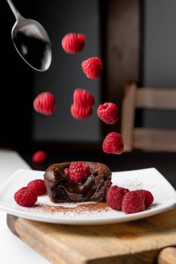 Fransız tatlısı, çikolata volkanı ya da pastanın yanında lezzetli erimiş çikolata. Tabağa bir sürü ahududu düşüyor.