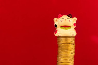 Maneki neko ya da bozuk para yığınına konmuş işaret eden kedi. Şansın, bolluğun ve ekonomik başarının kavramsal sembolü. Kırmızı arkaplan.