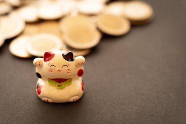 Maneki neko or beckoning cat, unfocused coins on the background. Conceptual symbol of luck, abundance and economic success. clipart