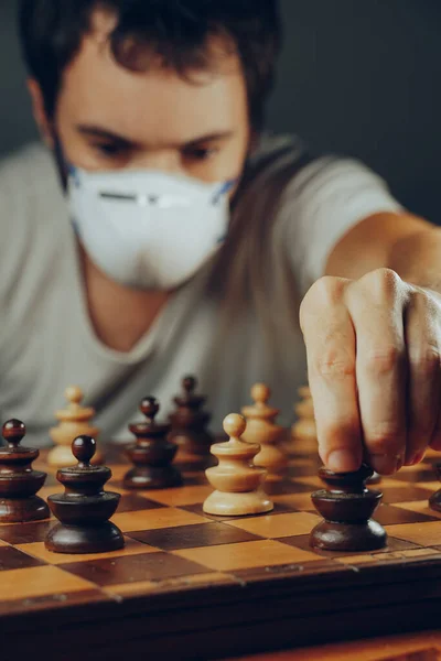 Social distancing in the 2019-ncov or coronavirus crisis. A man in a medical mask moves a token on a chess board full of pawns