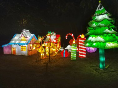 Noel Baba 'nın aydınlanmış figürü, kış mevsiminde Noel festivalinde gece vakti. Bir Noel geyiği ve kızağını resmeden ampullerden oluşan bir kompozisyon..