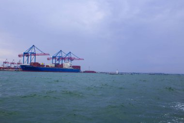 Odessa, Karadeniz 'deki akşam limanında portallar. Denize yanaşmış ağır bir yük gemisi. Arka planda konut ve ticari binalar bulunmaktadır.