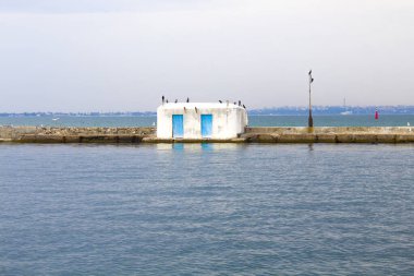 Rıhtımda bir bina. Ön planda körfez. Mavi gökyüzü ve su. Su evi, liman.