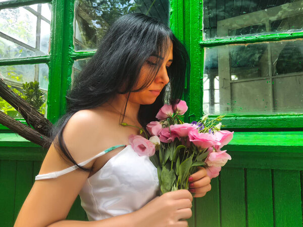 The beautiful girl in the hands of a pink bouquet of different flowers. Behind a background from green wooden boards