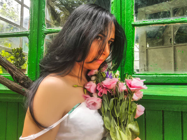 The beautiful girl in the hands of a pink bouquet of different flowers. Behind a background from green wooden boards