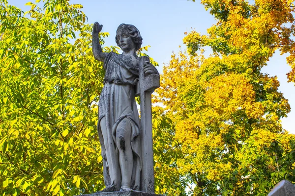 statue of kneeling angel with arms crossed against blue sky and cemetery headstone with crucifix background