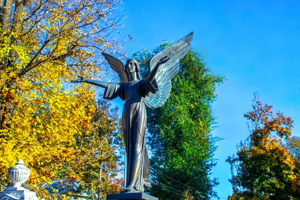 statue of kneeling angel with arms crossed against blue sky and cemetery headstone with crucifix background