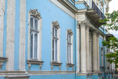 Eski bir malikanenin mavi duvarı kabartmalı çiçek desenleri ve sütunlu pencerelerle dekore edilmiş.