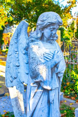 Kolları mavi gökyüzüne ve mezar taşına bağlı diz çökmüş haçlı bir melek heykeli.