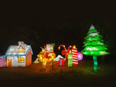 Noel Baba 'nın aydınlanmış figürü, kış mevsiminde Noel festivalinde gece vakti. Bir Noel geyiği ve kızağını resmeden ampullerden oluşan bir kompozisyon..