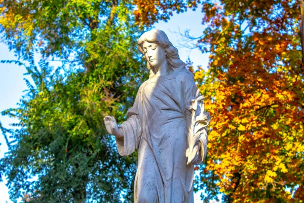 statue of kneeling angel with arms crossed against blue sky and cemetery headstone with crucifix background